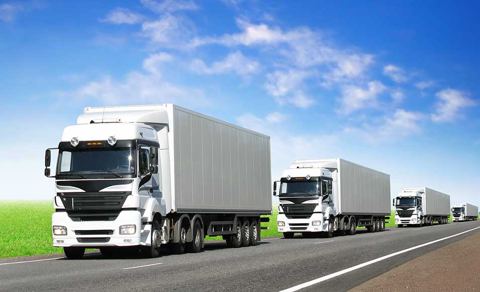 two white delivery trucks driving on a road